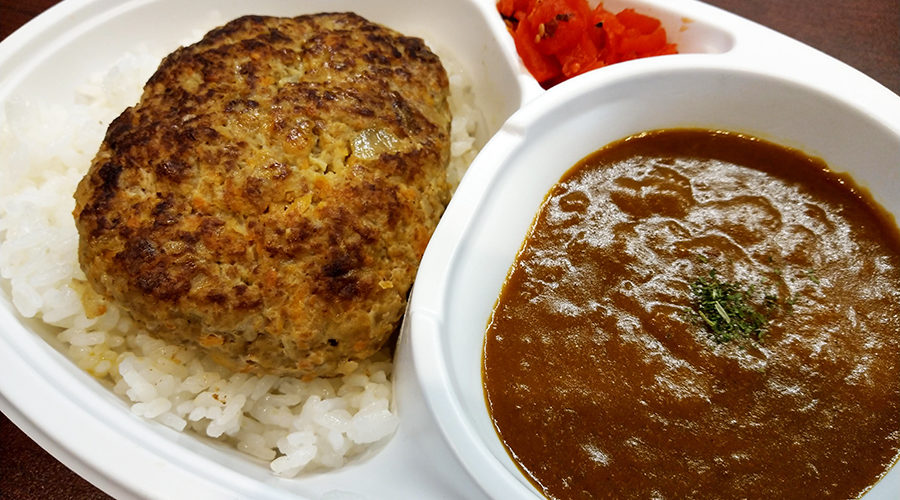 ご飯にのせた焼き色のついたパティと、茶色いカレーソース、角切りトマトが添えられた温かい色合いの一皿