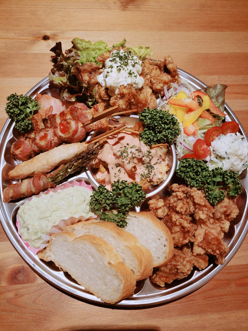 大皿に盛られた揚げ物や串焼き、サラダ、パンが並ぶ賑やかな食卓風景