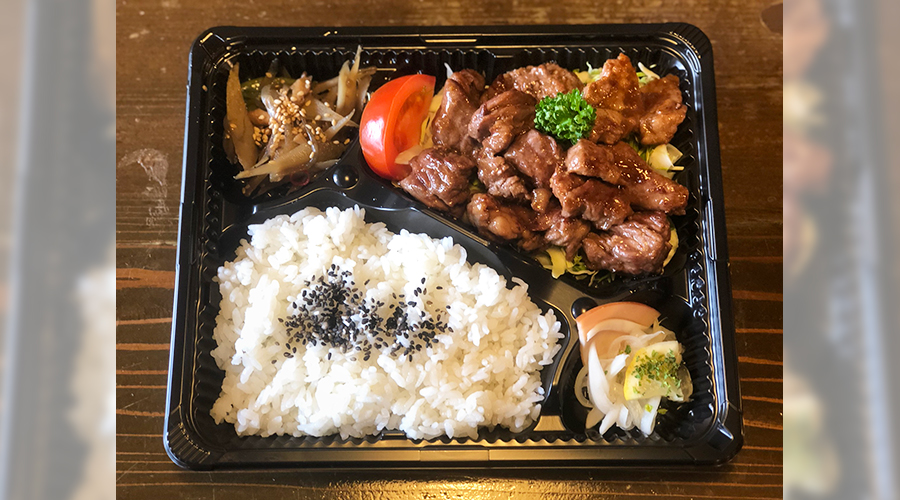 照り焼き風の肉料理と白ごまののったご飯、漬物とミニトマトが入った弁当の俯瞰