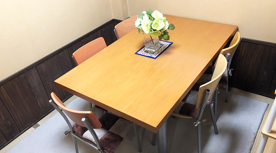 木製のテーブルとオレンジ色の椅子、花の飾りが置かれた落ち着いた雰囲気の小さな食事スペース